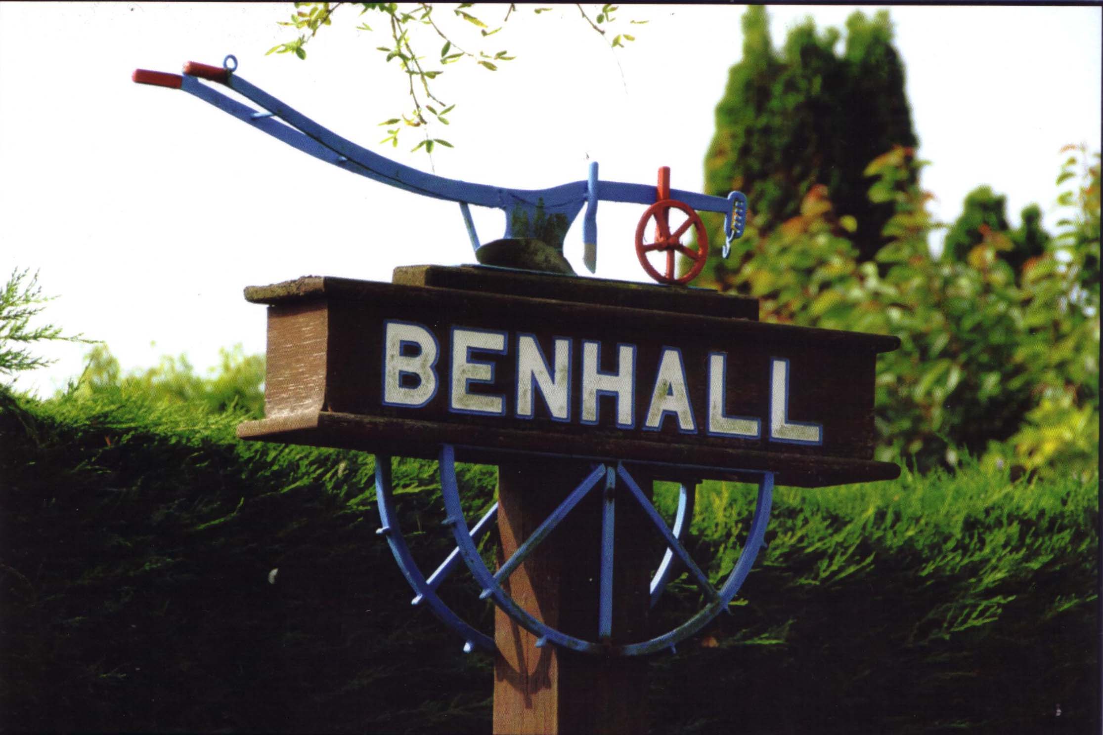 Benhall village sign in Cheltenham surrounded by greenery.