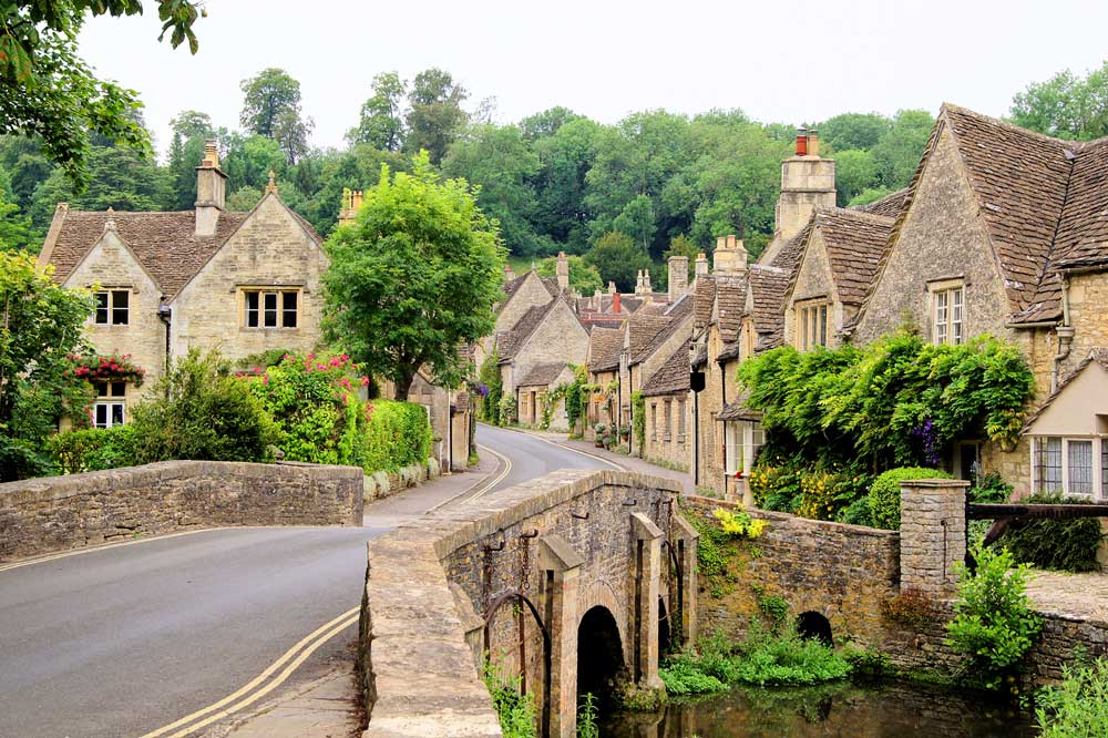 Scenic stone cottages and bridge in a traditional Cotswolds village surrounded by greenery.