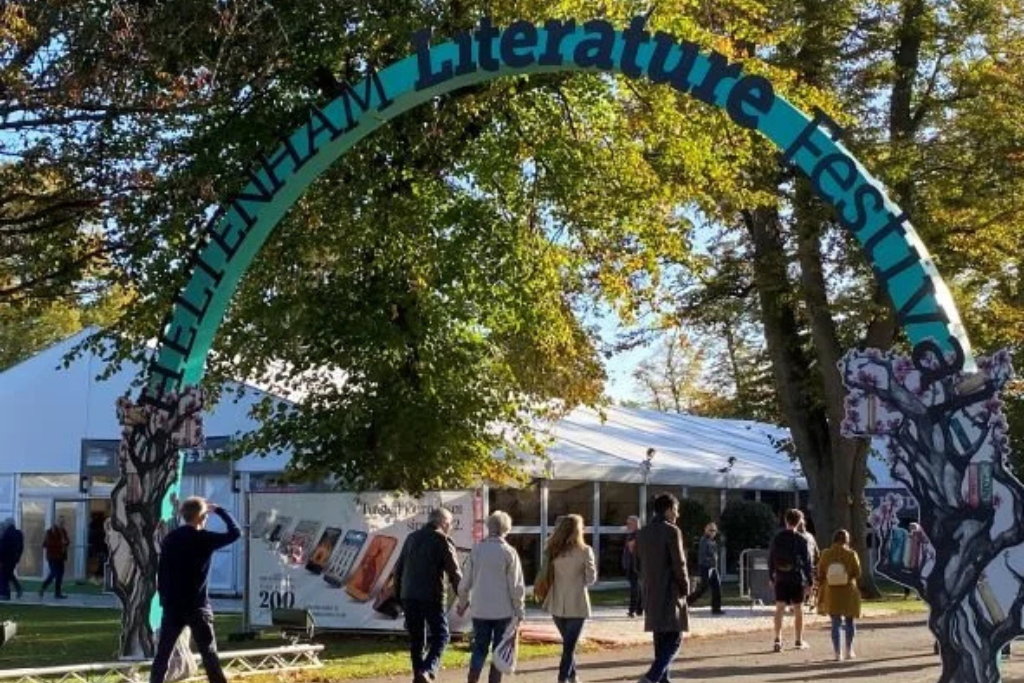 Entrance arch of the Cheltenham Literature Festival with visitors walking through the festival grounds.