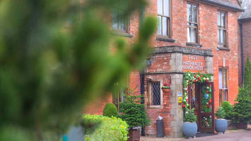 Exterior entrance of Hatherley Manor Hotel in Cheltenham surrounded by greenery.