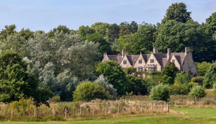 Asthall Manor surrounded by trees and open countryside in rural Oxfordshire on a clear day