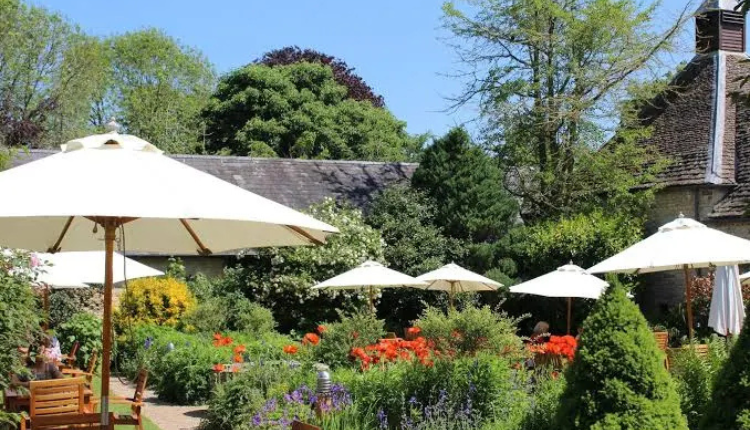 Garden terrace at The Lamb Inn in Burford with outdoor seating, white parasols, and colourful flowers