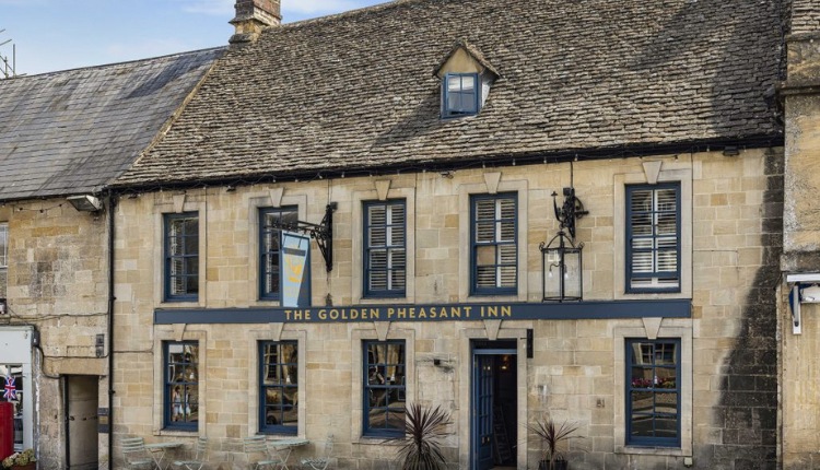 Front exterior of The Golden Pheasant Hotel in Burford, a traditional Cotswold stone inn with sash windows and flower displays