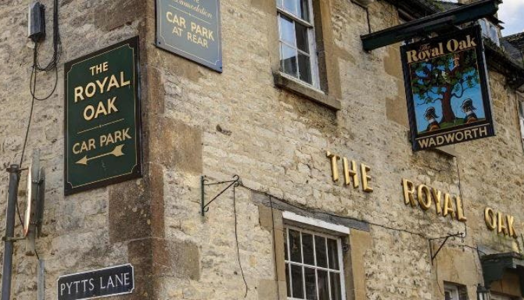 Exterior of The Royal Oak pub in Burford, a traditional Cotswold stone building with hanging pub signs and gold lettering