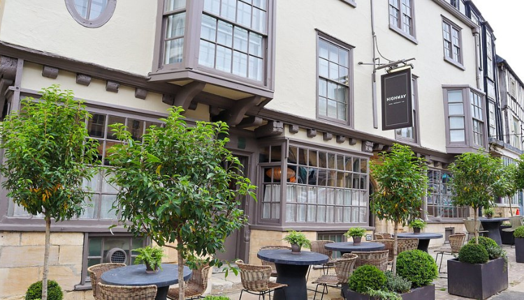 Exterior of The Highway Inn in Burford with stone façade, bay windows, and outdoor seating with potted trees