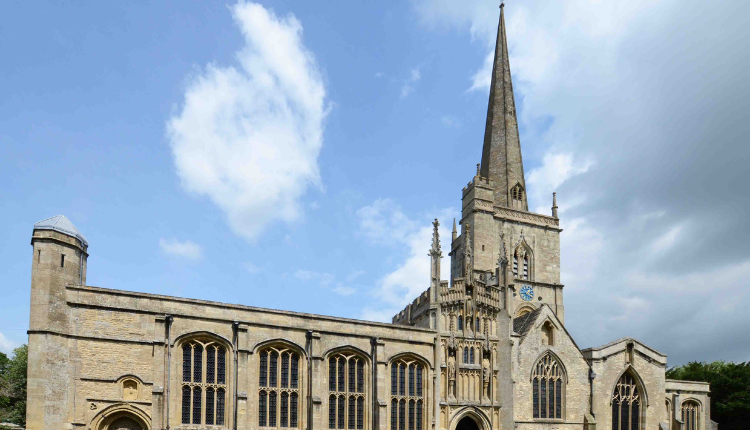 St John the Baptist Church in Burford with tall spire, Gothic stone architecture, and historic gravestones in the churchyard