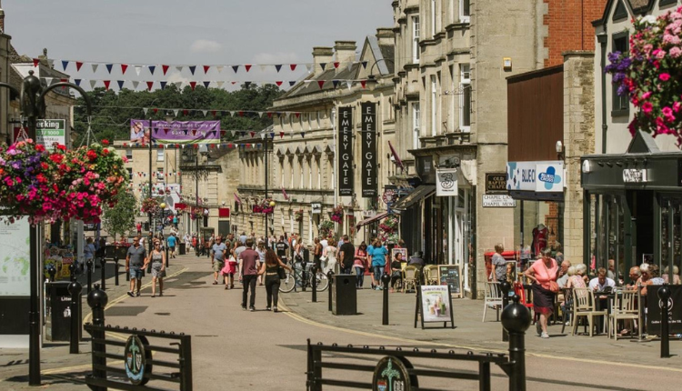 Chippenham town centre with busy high street, shops, cafés, pedestrians, and hanging flower baskets in Wiltshire