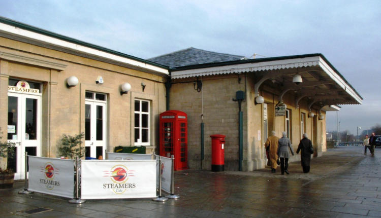 Chippenham railway station exterior with café seating, red telephone box, and passengers walking along the platform area