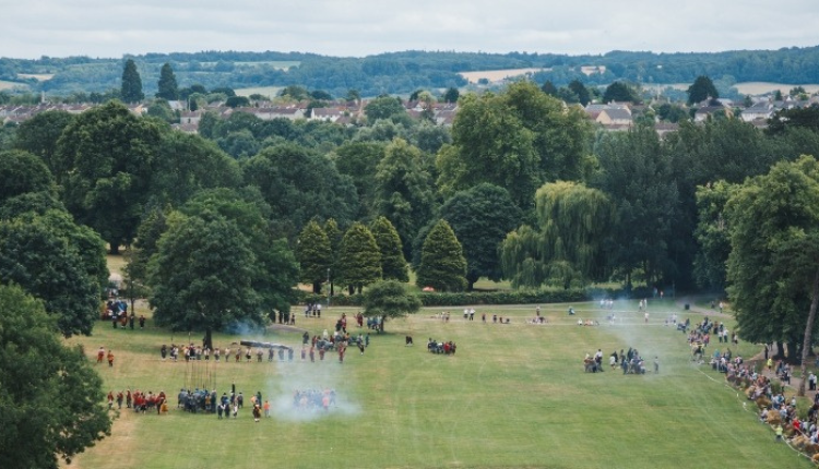 Aerial view of Monkton Park in Chippenham showing large green open fields, mature trees, and crowds gathered for an outdoor event