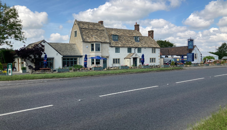 Traditional stone-built pub and houses along a roadside in Pewsham, Wiltshire, under a blue sky with scattered clouds