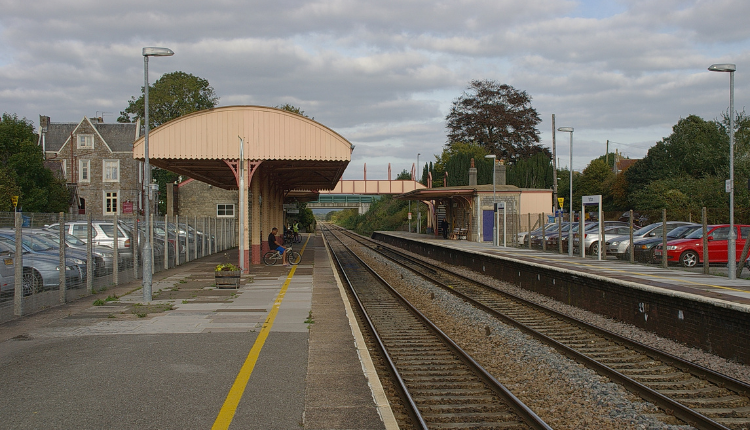 Yatton railway station platform with tracks, traditional canopy, and parked cars beside the station
