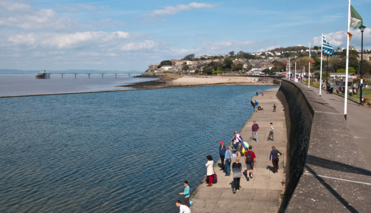 People walking along Clevedon Seafront promenade with sea wall and Clevedon Pier in the distance