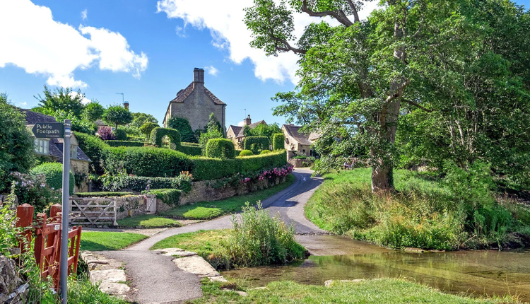 Footpath crossing a shallow stream with stone cottages in Upper Slaughter, Cotswolds