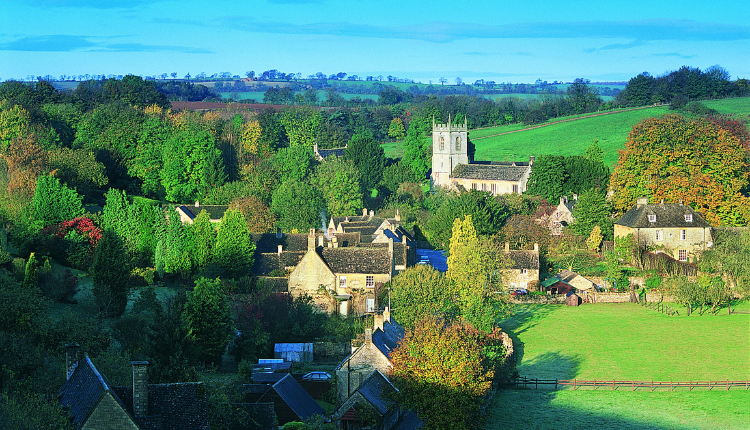 Aerial view of Naunton village with stone cottages, church, and rolling green countryside in the Cotswolds