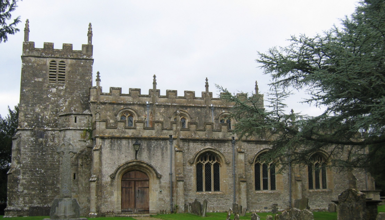 Historic stone church in Cold Aston village surrounded by gravestones and green lawns in the Cotswolds