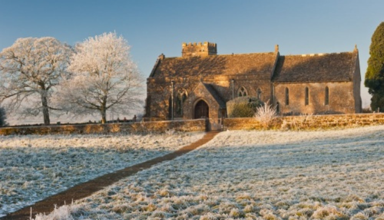 Stone church in Lower Rissington surrounded by frost-covered fields and winter trees in the Cotswolds