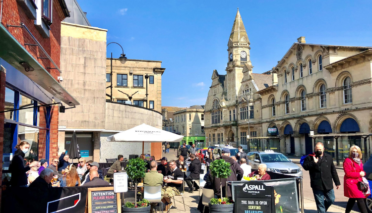 Busy Trowbridge town centre with outdoor café seating and the historic Town Hall clock tower under a clear blue sky