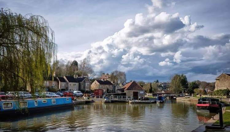 Canal boats moored along the Kennet and Avon Canal in Hilperton village with stone houses and dramatic clouds overhead
