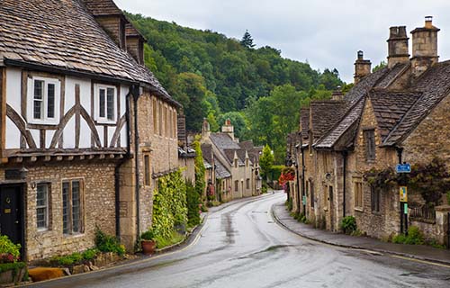 Curving village road lined with historic Cotswold stone cottages near Chippenham, surrounded by greenery