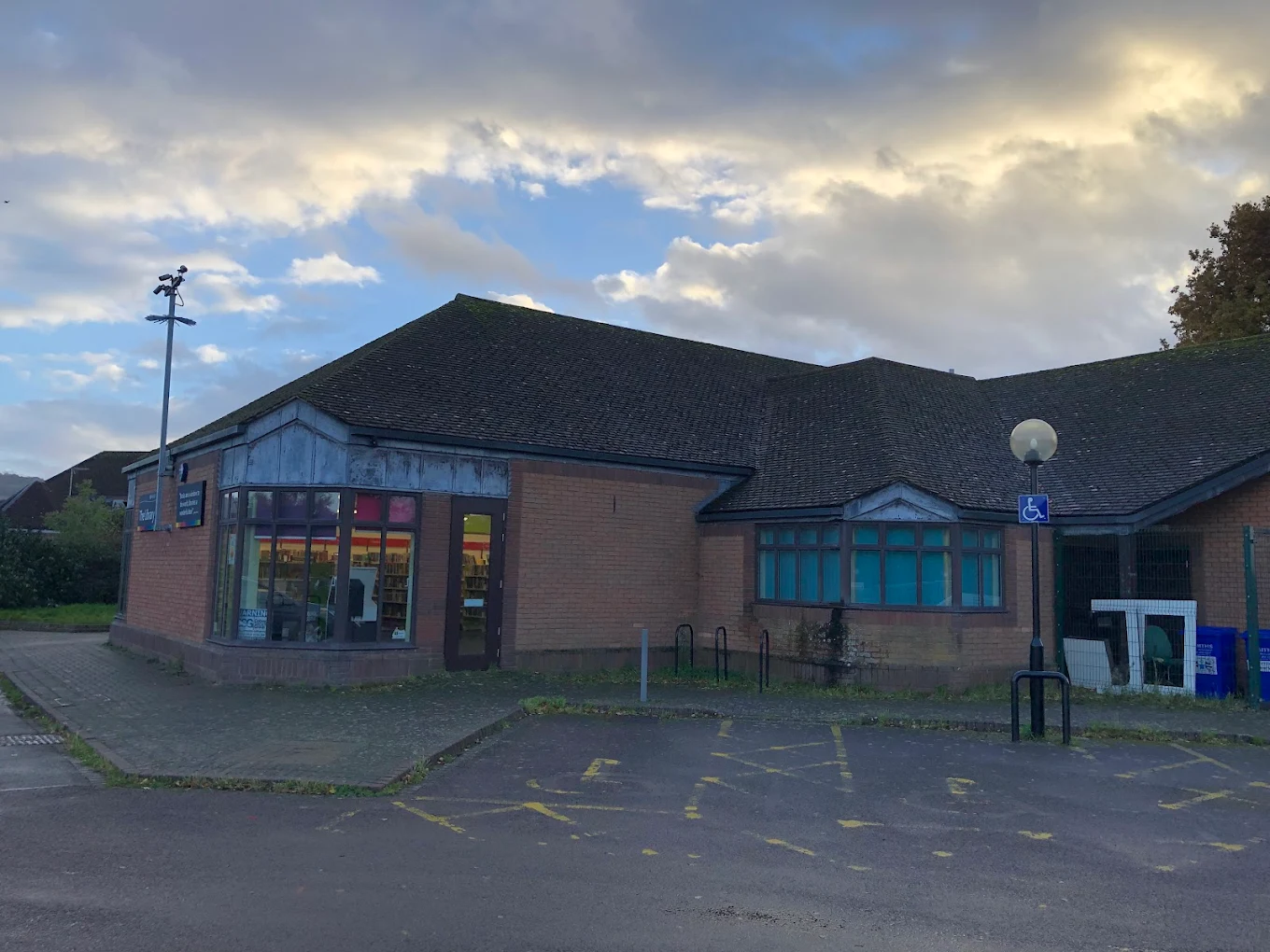 Community building in Up Hatherley, Cheltenham, with a car park and cloudy sky.