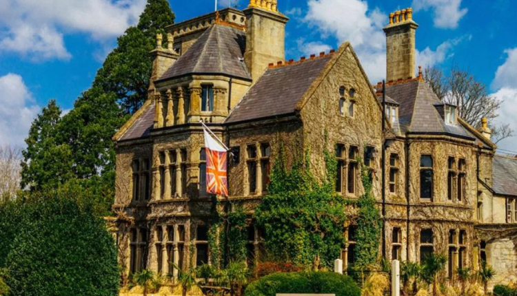 Historic stone manor house in Rudloe, Wiltshire, surrounded by greenery under a blue sky