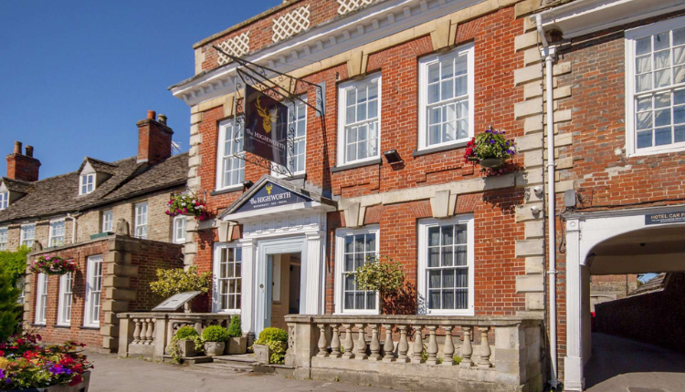 The Highworth Hotel in Highworth, a traditional red-brick hotel building with white-framed windows and hanging flower baskets.