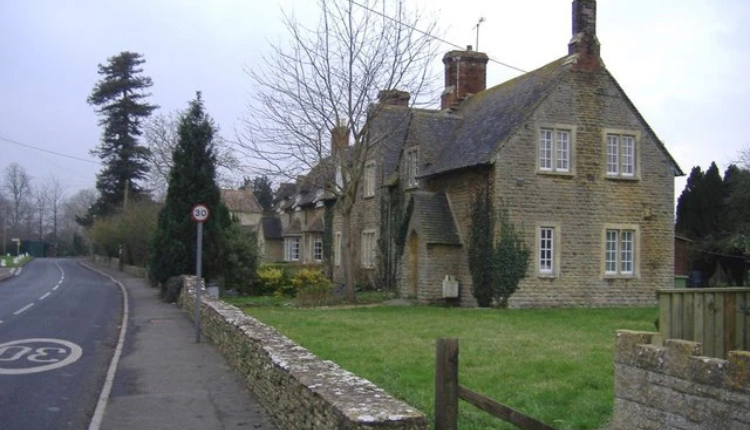 Historic stone church with a tall spire in Down Ampney, surrounded by gravestones and green churchyard.