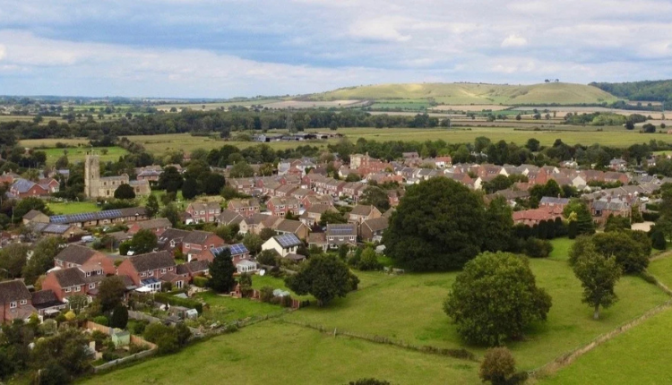 Aerial view of the village of Rowde in Wiltshire with houses, church tower, green fields and rolling countryside
