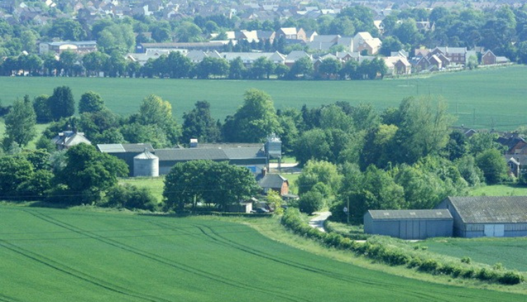 Rural view of Roundway in Wiltshire with green farmland, farm buildings and village housing in the distance