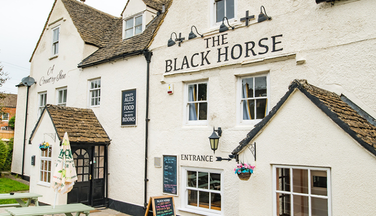 Exterior of The Black Horse Inn in North Nibley, a traditional white-painted country pub with pitched roofs and hanging signage.