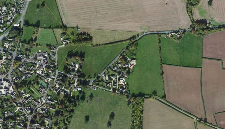 Aerial view of Kemble near Fairford showing village housing, roads, and surrounding farmland.