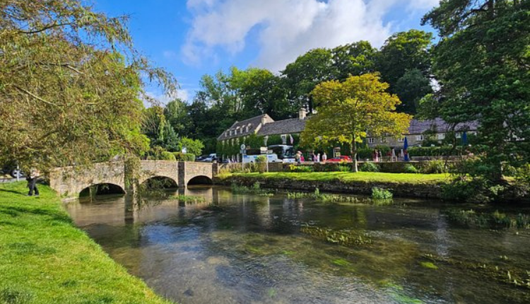 Stone bridge over the River Coln in Coln St Aldwyns with cottages and trees.