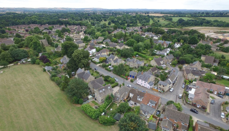 Aerial view of Watchfield village showing Cotswold-style houses, surrounding fields, and green countryside.